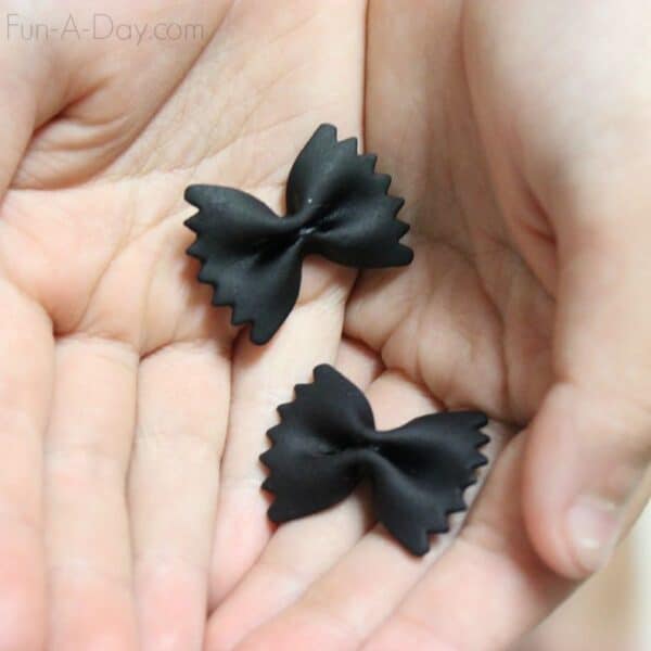 child's hands holding two bowtie pasta pieces dyed black for sensory play