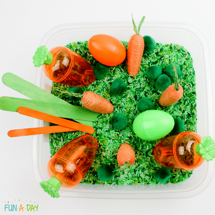 dyed green rice with toy carrots, craft sticks, pompoms and plastic eggs