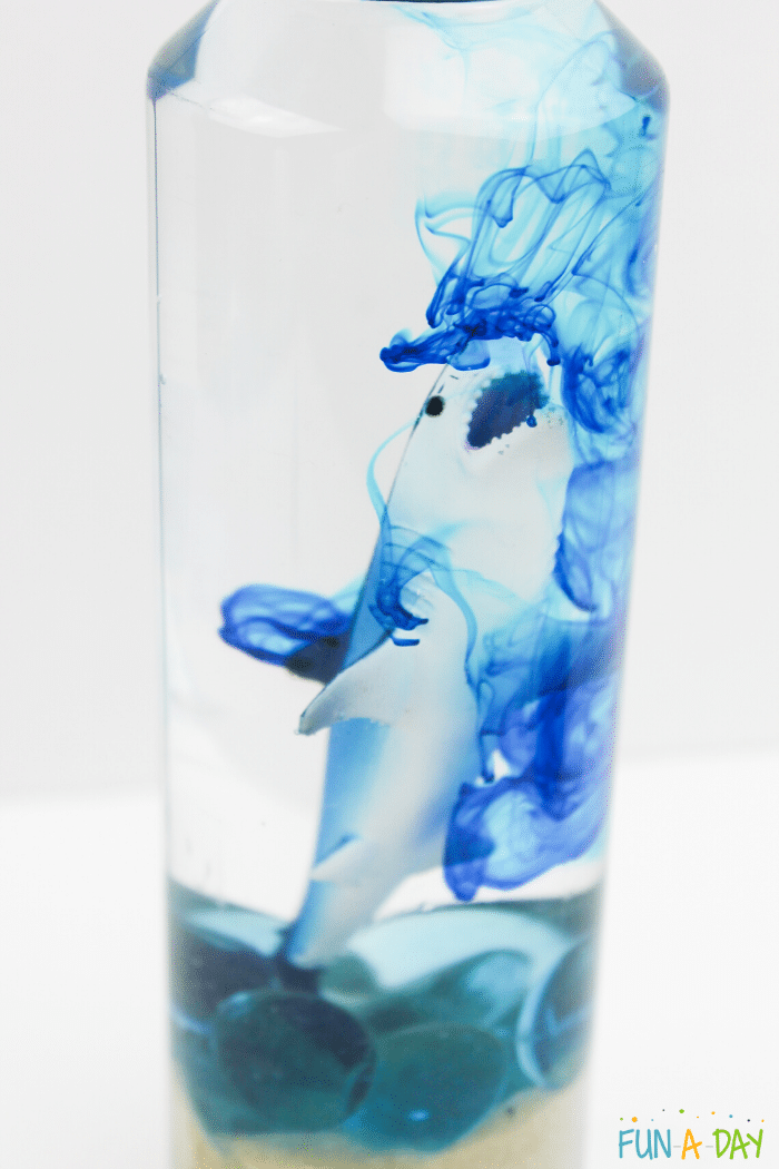 shark, sand, and glass gems in a plastic bottle with blue tinted water