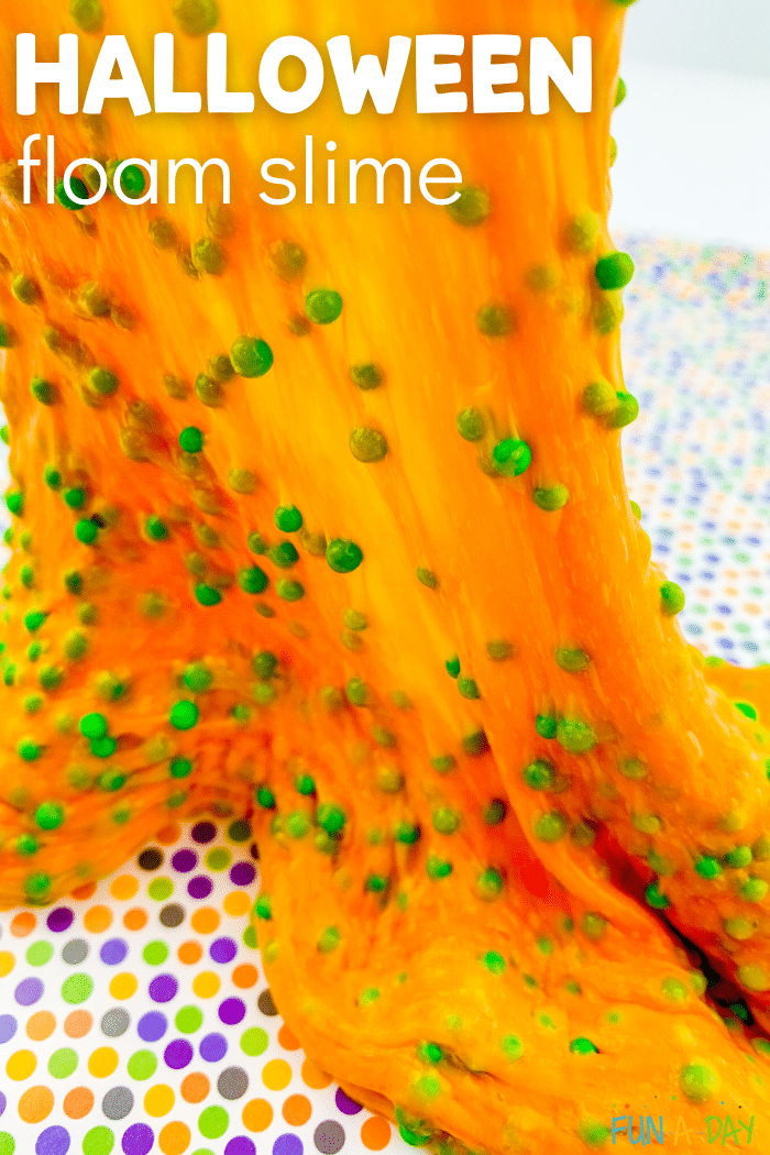 Orange slime with green foam beads being stretched away from multicolored polka dot crafting mat. Text that reads Halloween foam slime.