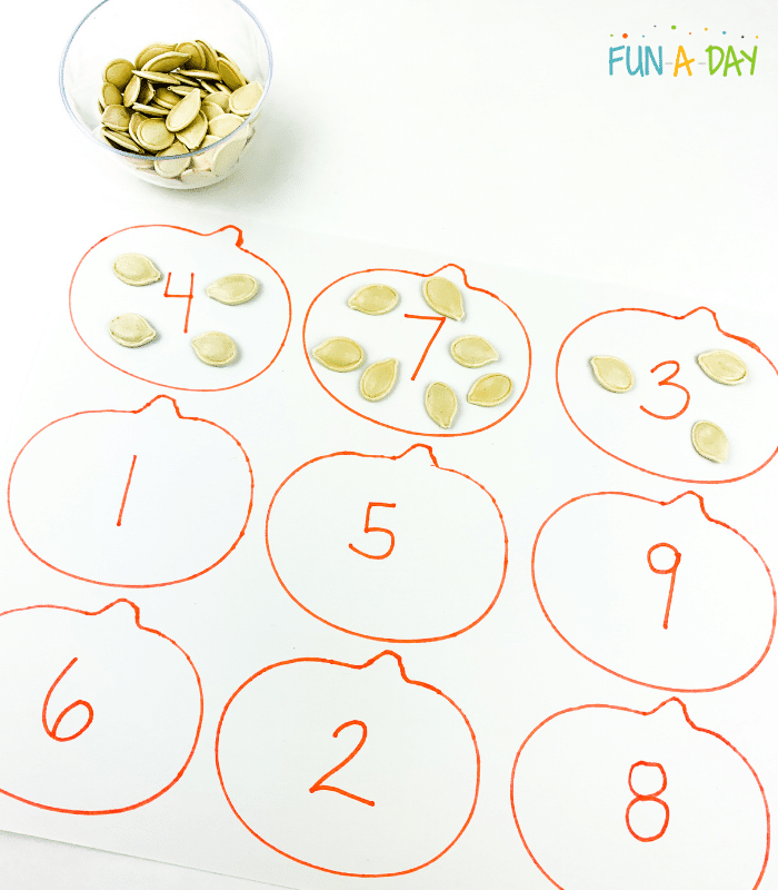 Outlined pumpkins with numbers written in them, small bowl of pumpkin seeds, pumpkin seeds placed on pumpkin according to number.