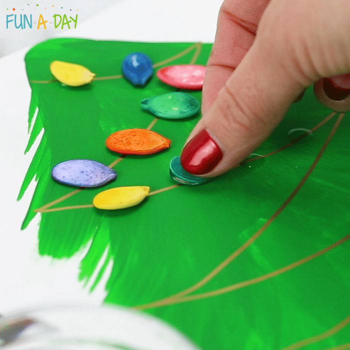 fingers adding dyed pumpkin seeds to christmas tree art