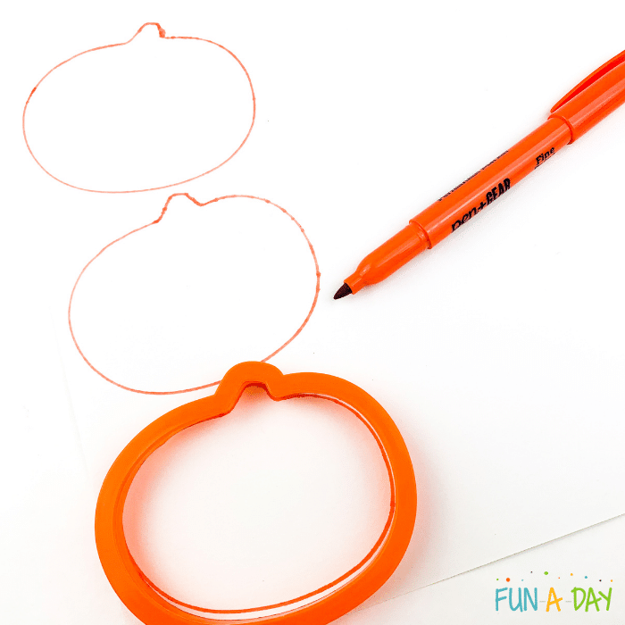 Orange pumpkins being traced on white paper using orange marker and orange cookie cutter.