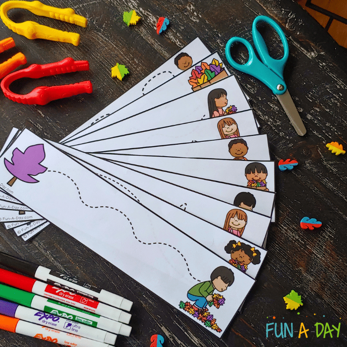 Preschool fall cutting strips surrounded by scissors, leaf mini erasers, dry erase markers, and tongs.