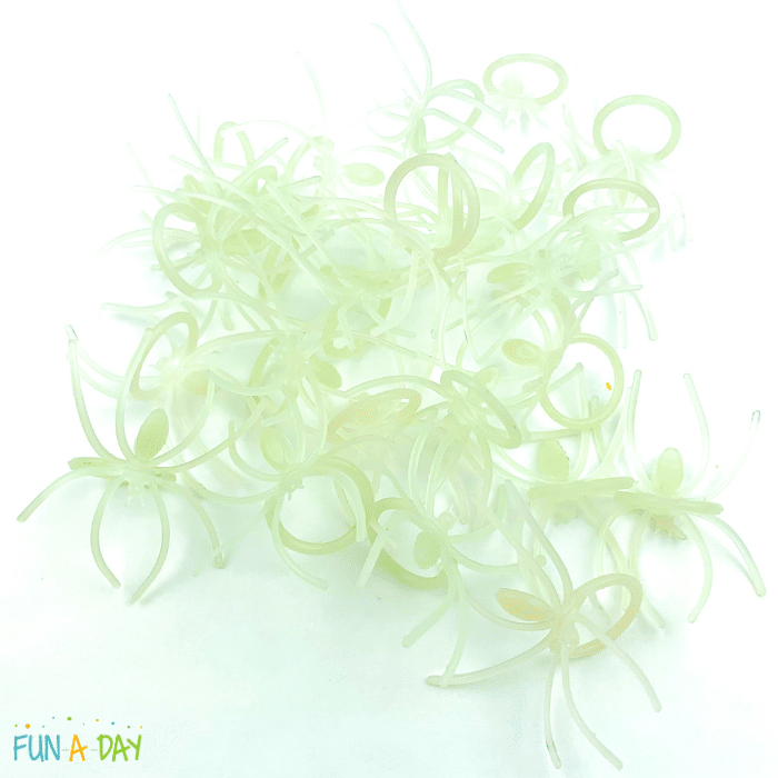 Pile of muted green glow in the dark spider rings on white background.