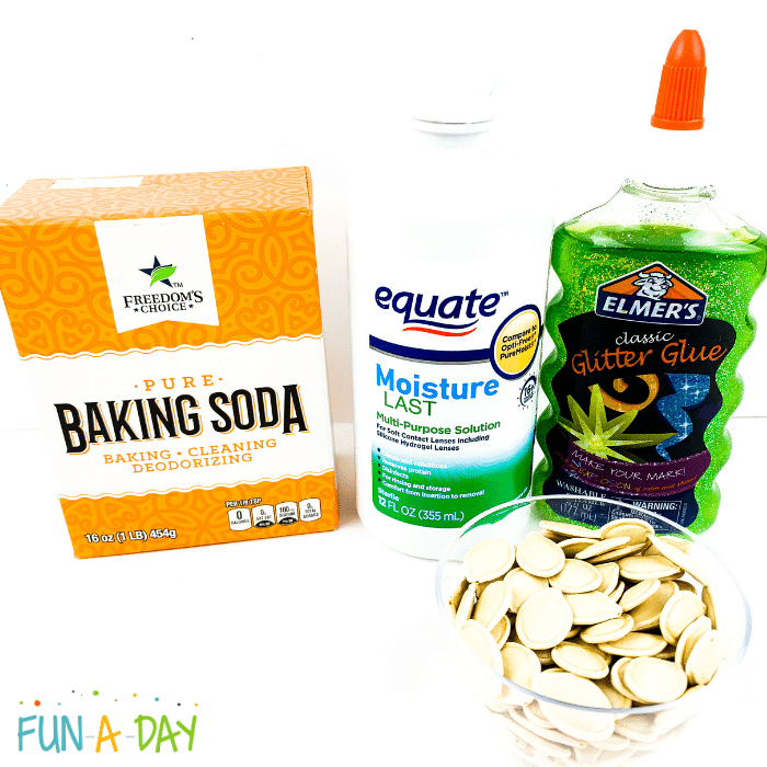 Baking soda, contact solution, green glitter glue, and small bowl of pumpkin seeds.