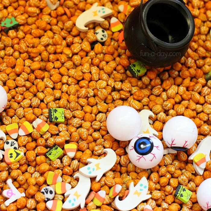 orange dyed chickpeas with mini erasers and halloween toys in a sensory bin