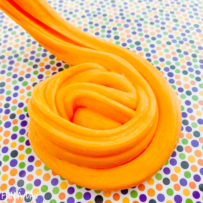 Orange slime being twirled into a spiral shape on a multicolored polkadot craft mat.