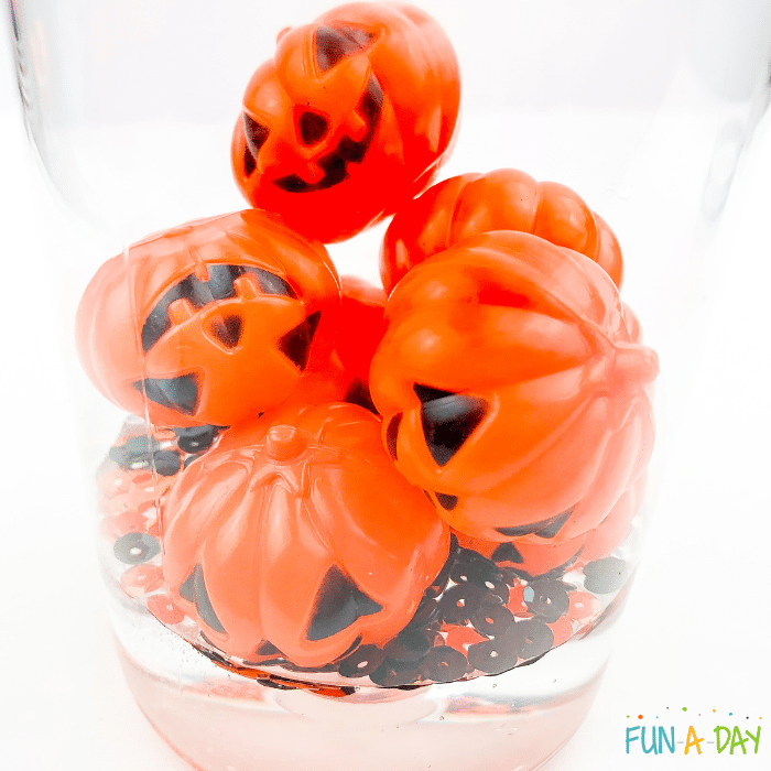 Clear plastic bottle with black and orange sequins and jack-o-lanterns sitting on top of clear glue.