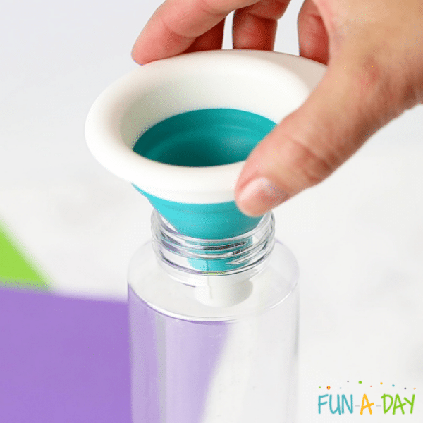 Hand placing funnel into clear bottle.