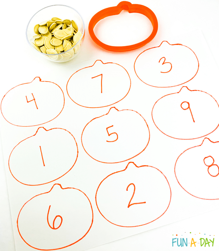 Small bowl of pumpkin seeds, pumpkin cookie cutter, and traced pumpkins with numbers in them.