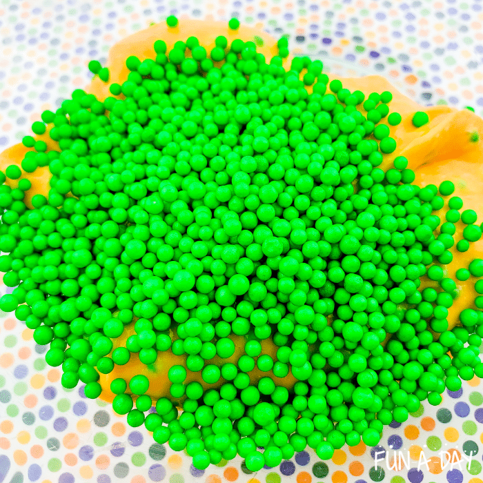 Green foam beads poured out on top of the orange slime.
