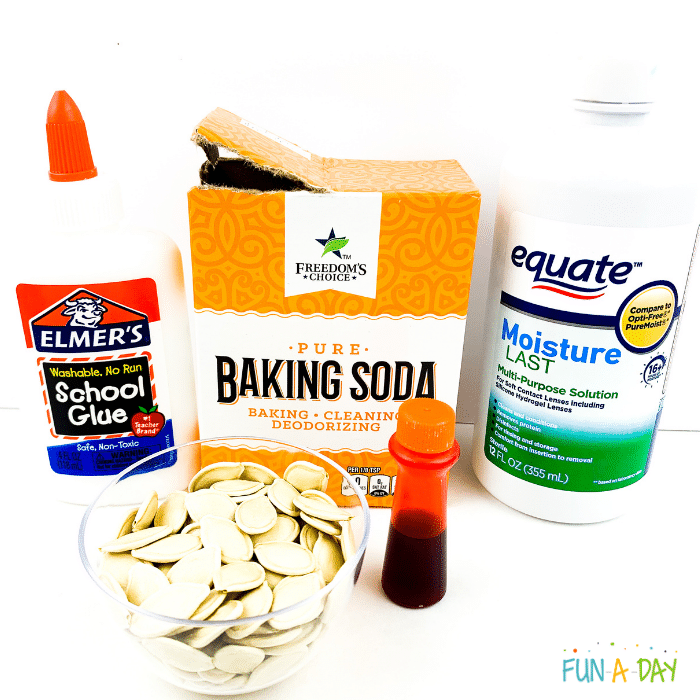 Elmer's glue, baking soda, contact solution, orange food dye, and small bowl of pumpkin seeds.