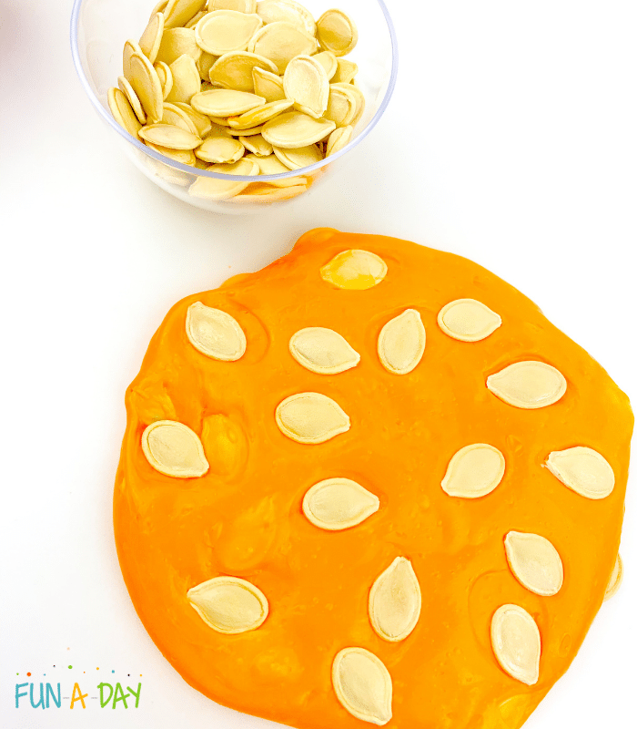 Orange slime with pumpkin seeds and extra pumpkin seeds in small bowl.