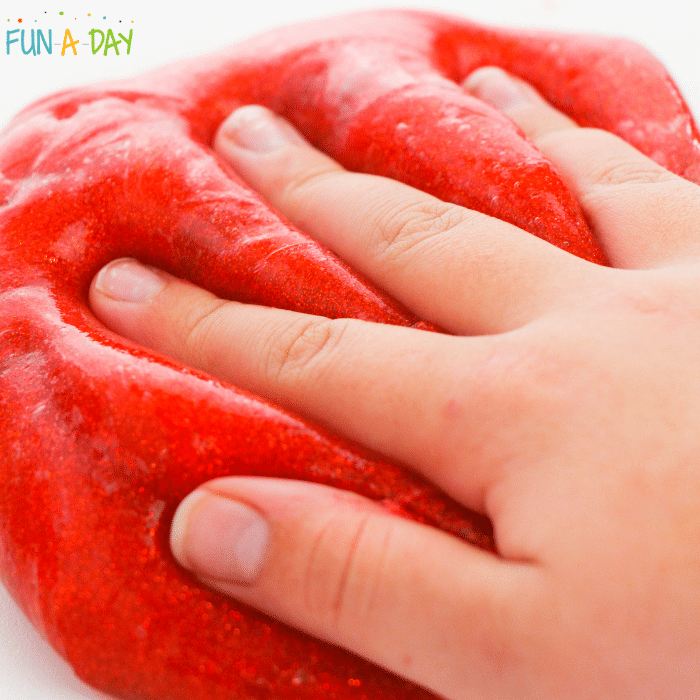 Hand pressing into red glittery slime.