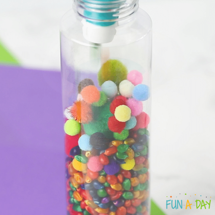 Rainbow corn sensory bottle with colorful pompoms.
