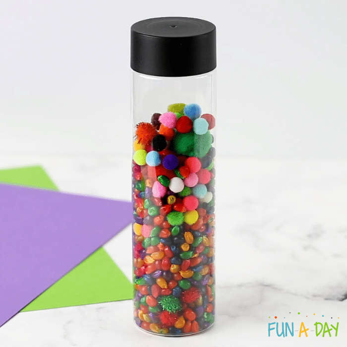 Image of clear bottle with multi-colored corn kernels and pompoms.