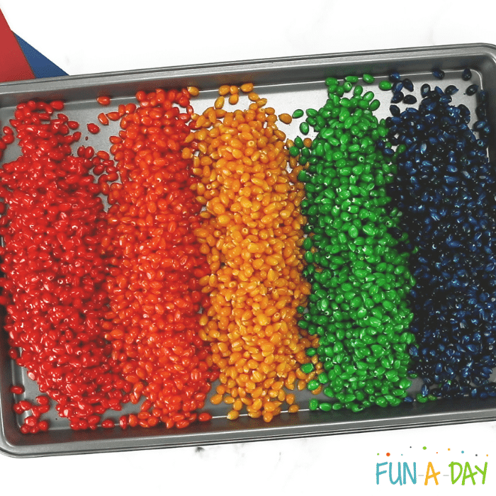 Cookie sheet with a line of red, orange, yellow, green, and then blue corn kernels.