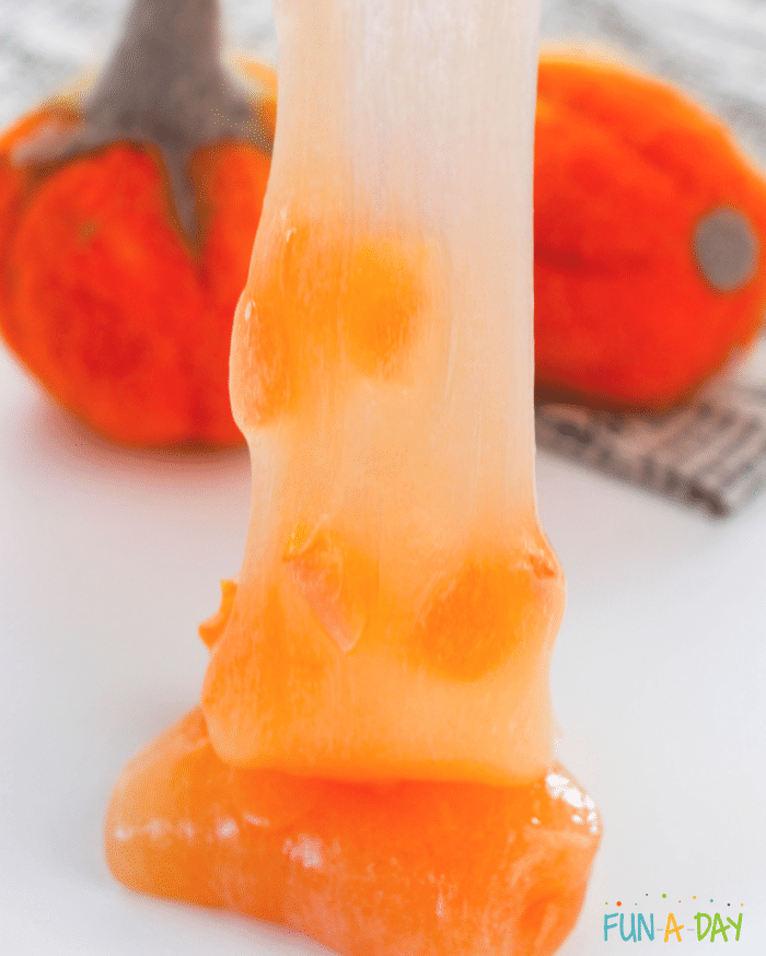 Light orange slime with pumpkin glitter being stretched.