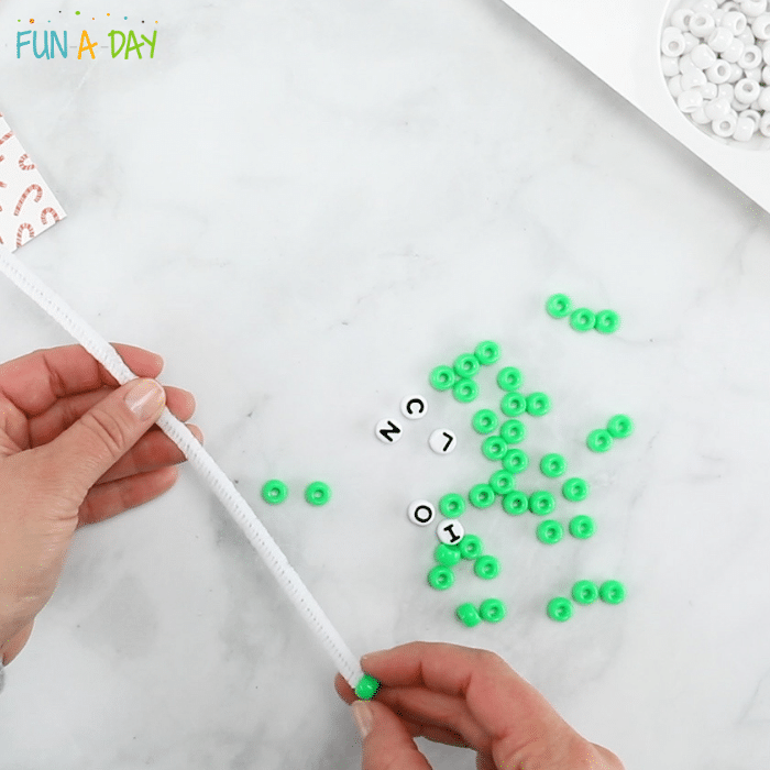 Adding green beads to white pipe cleaner.