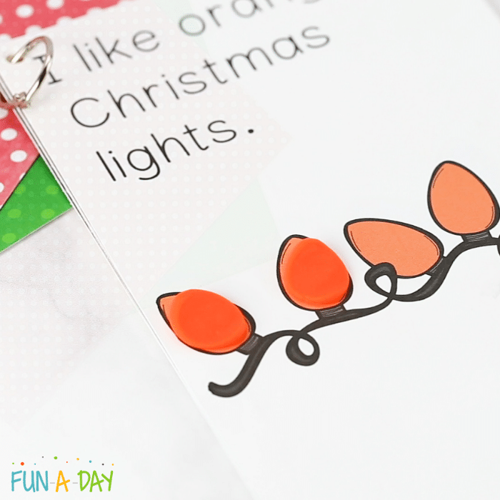 Laminated page from Christmas lights printable book that reads 'I like orange Christmas lights' with orange Play dough pieces on the lights.