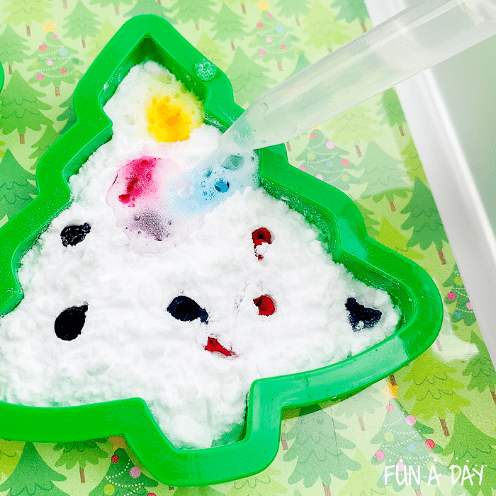 Dropper putting vinegar on top of baking soda and food coloring dots inside of a Christmas tree cookie cutter.