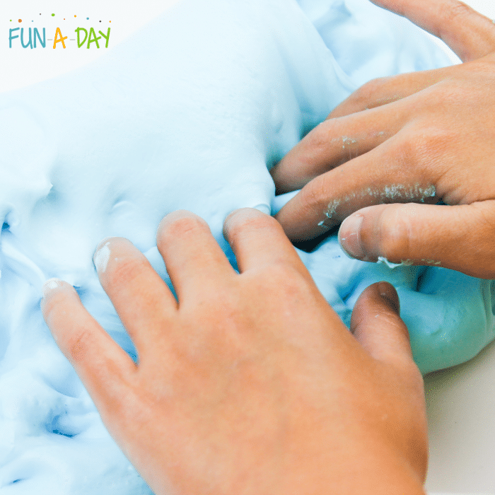Hands poking into blue fluffy slime.