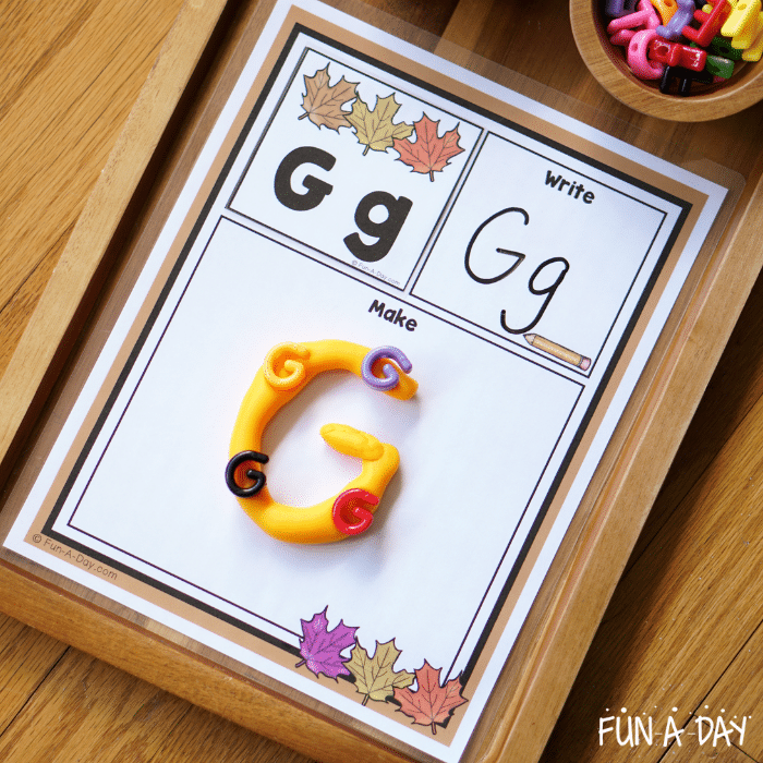 Letter Gg alphabet card on fall read it, write it, build it mat. G made in orange play dough on mat, with G letter beads.