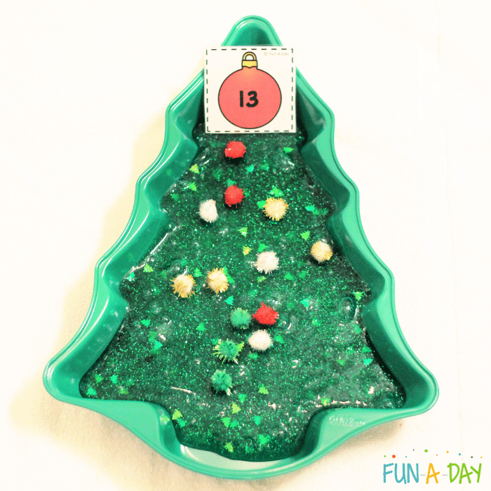 Green glitter slime in a tree-shaped pan with pompoms and printable number card.