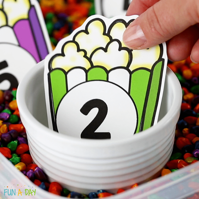 Number two corn counting card in small bowl surrounded by colorful corn kernels.
