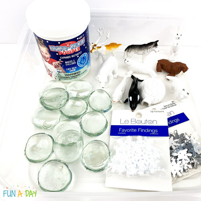 Materials needed for the Arctic sensory bin, including a bin, clear gems, insta-snow powder, arctic animal toys, and snowflake confetti.