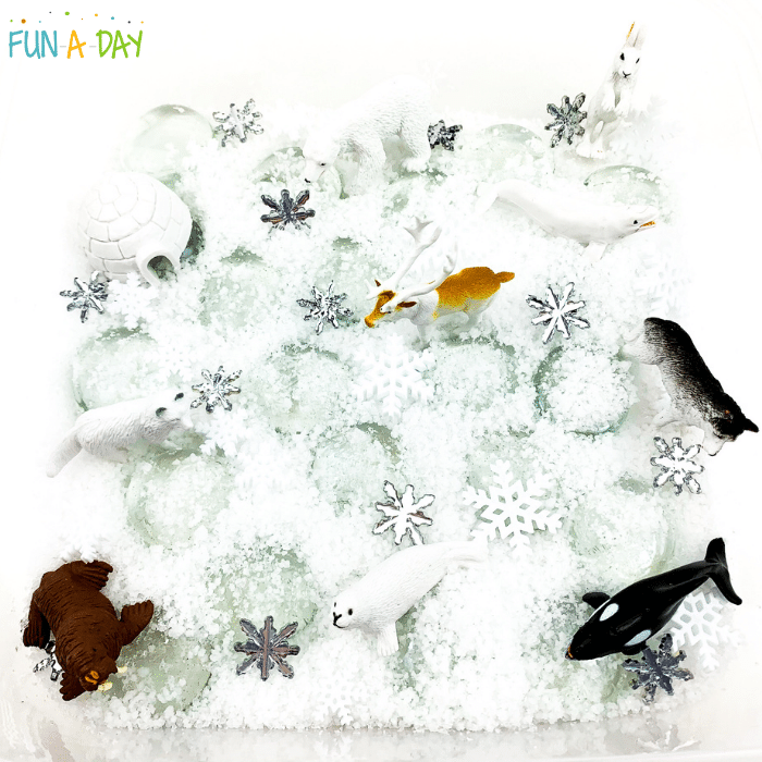 Arctic sensory bin with insta-snow, clear gems, a toy igloo, and toy arctic animals.