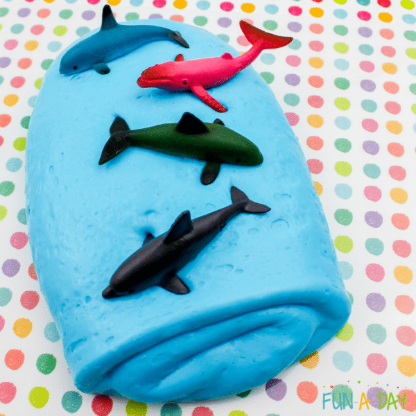Blue ocean slime folded into a pile with toy whales, dolphins, and sharks on top.