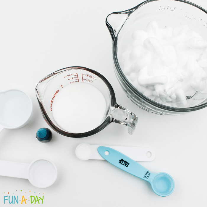 Ingredients for ocean slime which include glue, contact solution, water, baking soda, shaving cream, and a container of neon blue food dye.