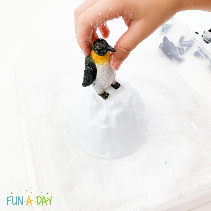 Hand placing penguin on top of snow molded into a castle.