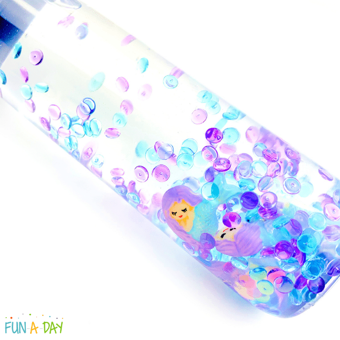 Sensory bottle with mermaid charms and fishbowl beads floating in clear liquid.