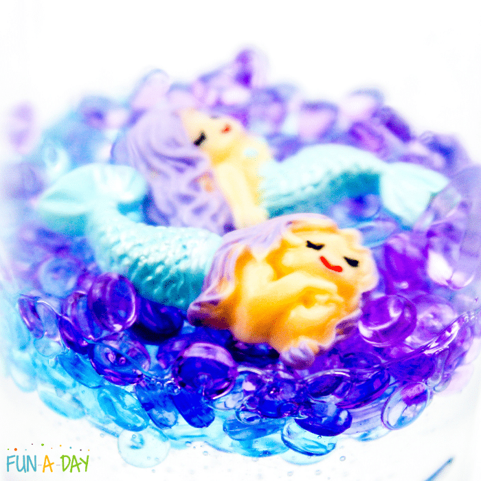 Mermaid charms resting on fish bowl beads in a sensory bottle.