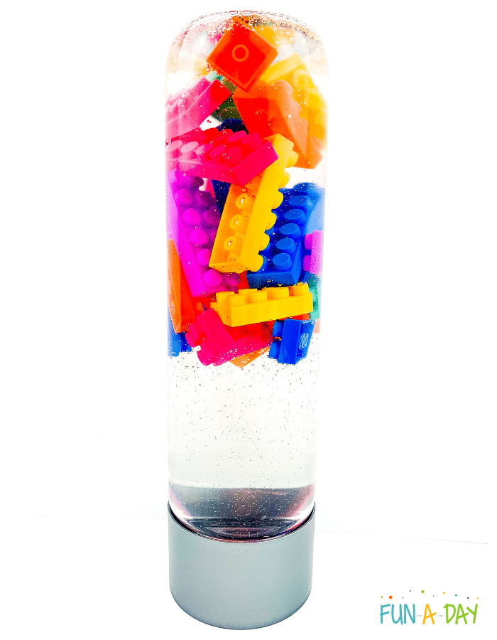 Clear bottle sat upside down with brightly colored legos floating in clear liquid.