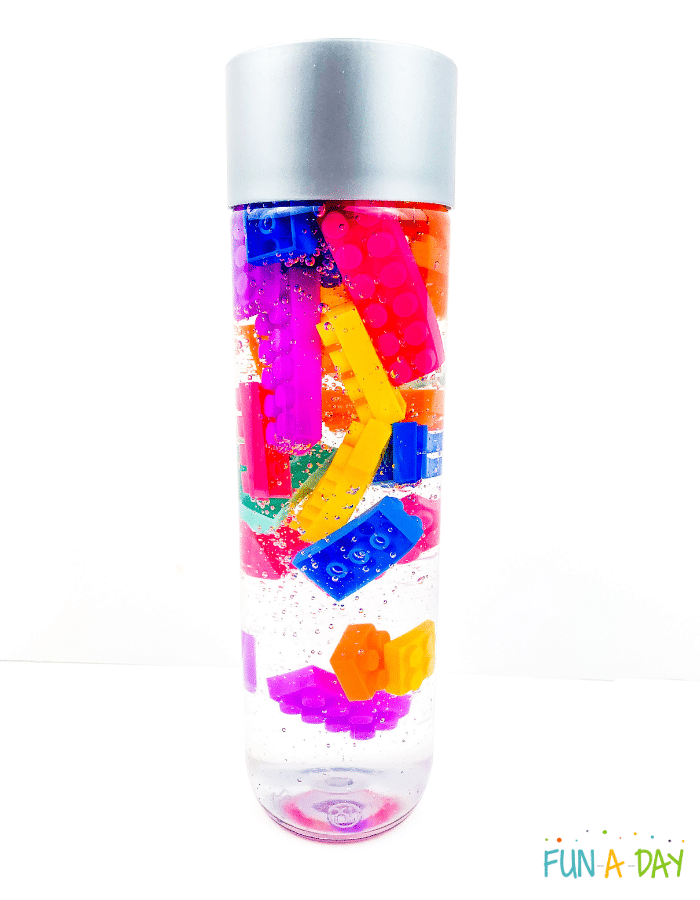 Clear sensory bottle with vibrantly colored legos floating around.