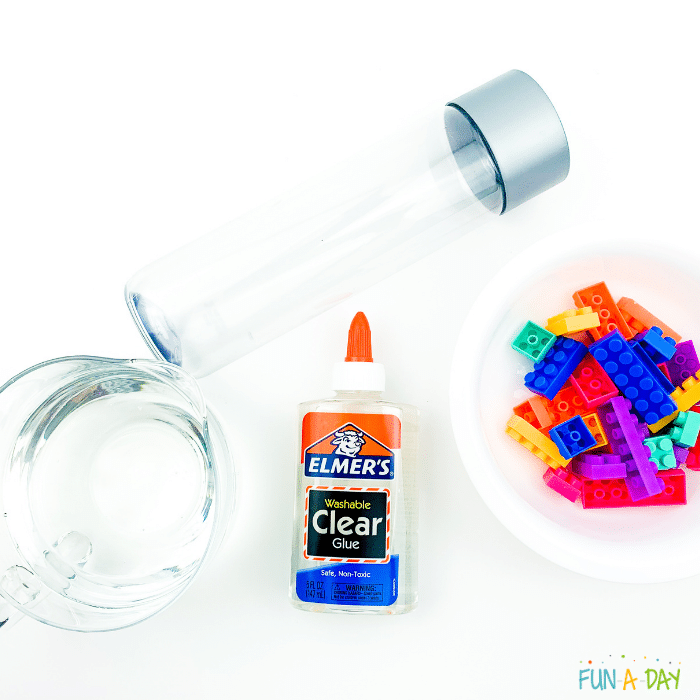 Materials needed for the Lego sensory bottle which include water, Elmer's clear glue, clear sensory bottle and brightly colored plastic bricks.