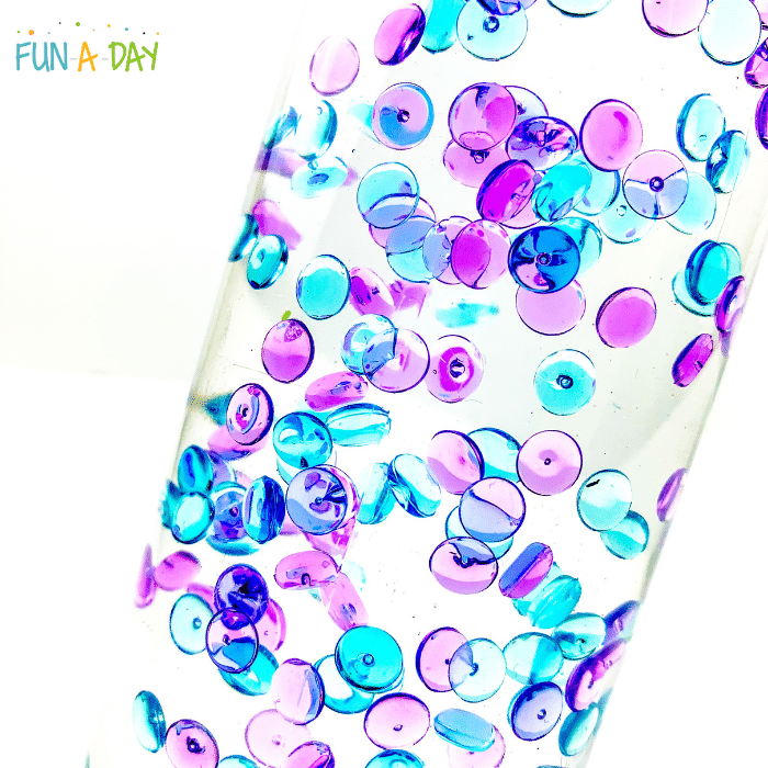 Blue and purple fish bowl beads floating in the clear liquid of a sensory bottle.