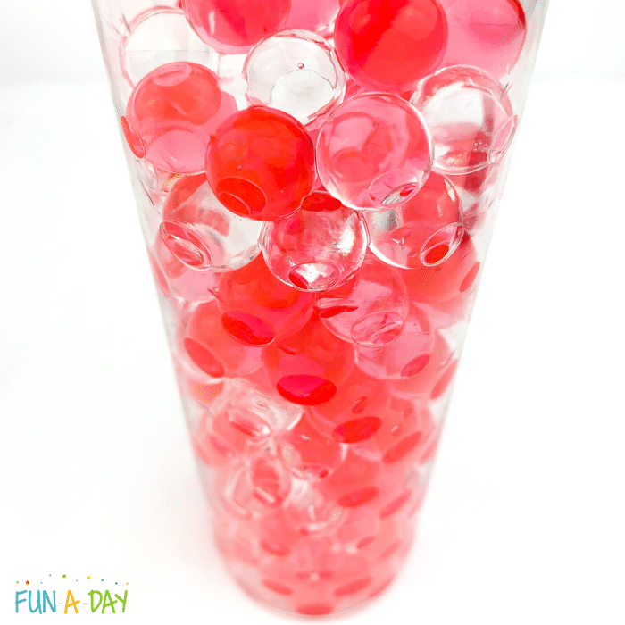 Clear bottle full of expanded red and clear water beads.