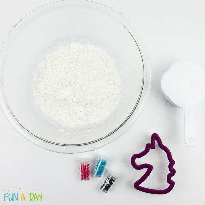Ingredients for unicorn dough which includes corn starch, conditioner, unicorn cookie cutter, and turquoise, pink, and silver glitter.