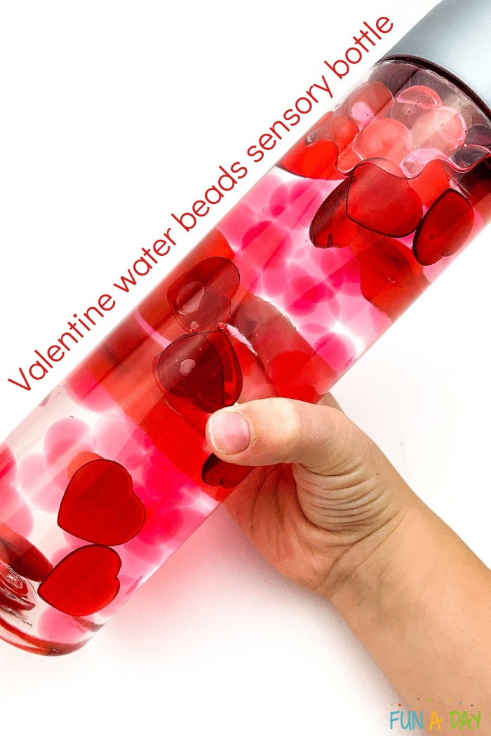 Child's hand holding valentine sensory bottle with text that reads valentine water beads sensory bottle.