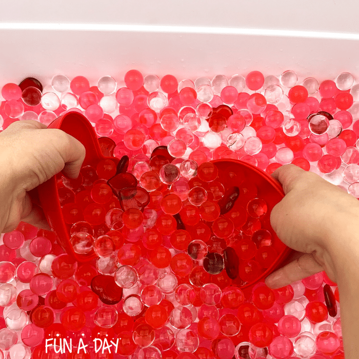 child using a heart container to scoop water beads in valentine's day sensory bin