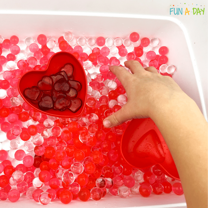 child's hand playing in water bead valentine sensory bin