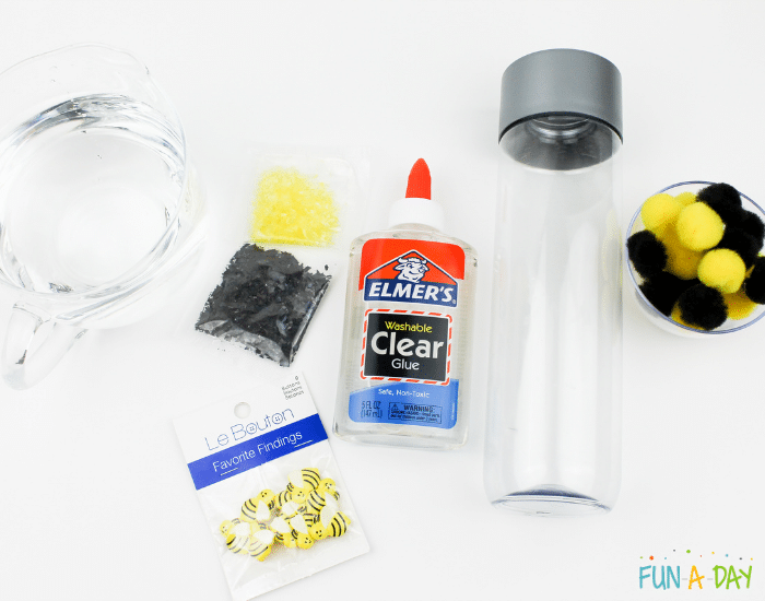 Ingredients used to make the bee sensory bottle which include warm water, clear glue, black and yellow foil confetti, black and yellow pompoms, bee buttons, and clear sensory bottle.