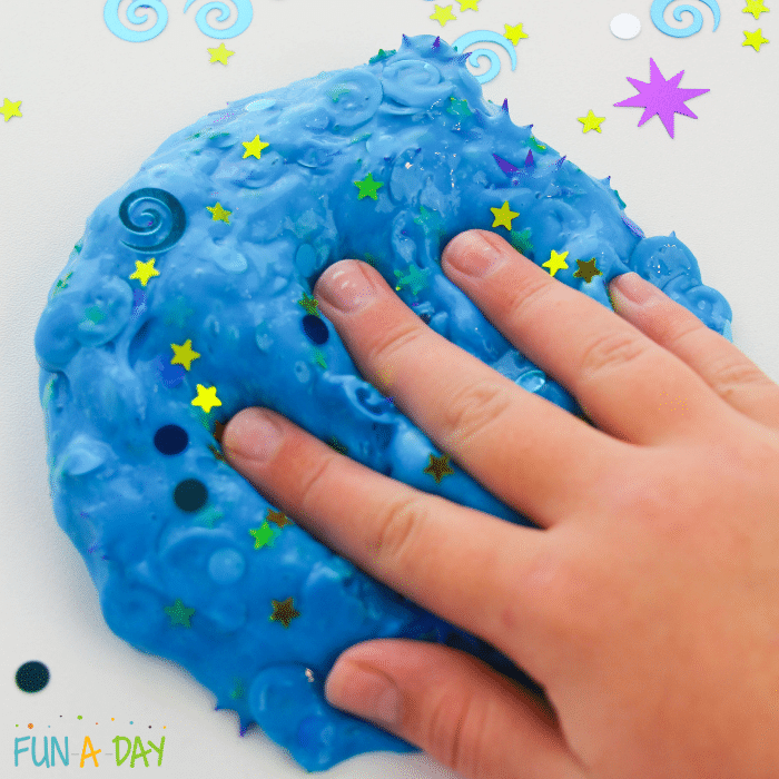 child's hand pressing into blue confetti slime