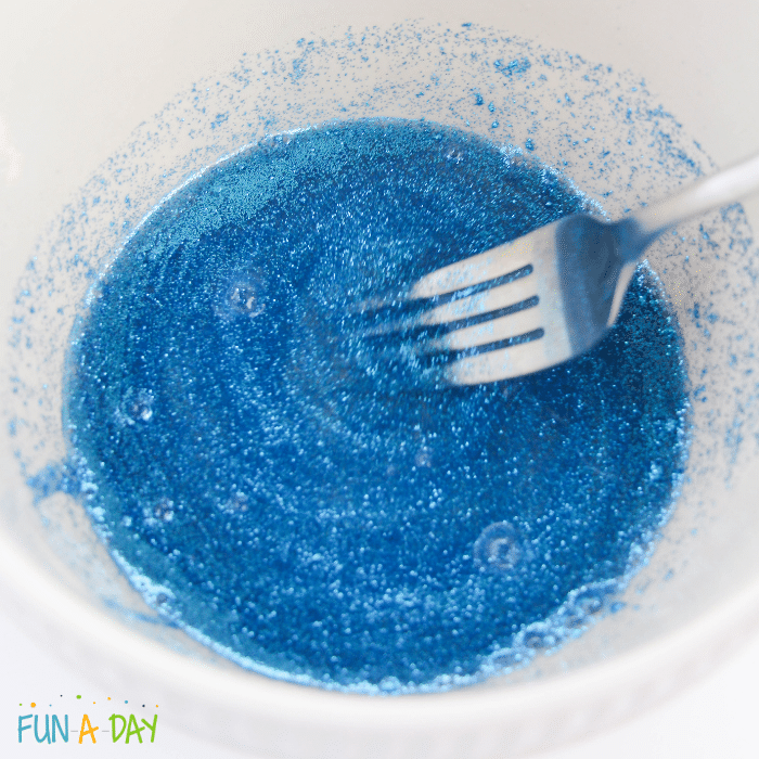 Fork mixing blue glitter into slime mixture.