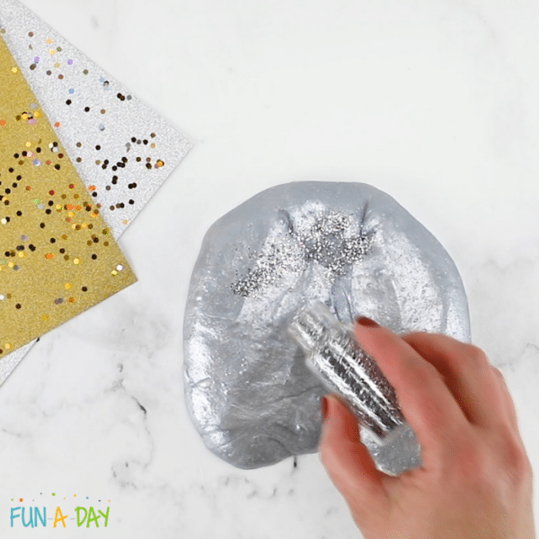 Hand adding silver glitter to silver slime.
